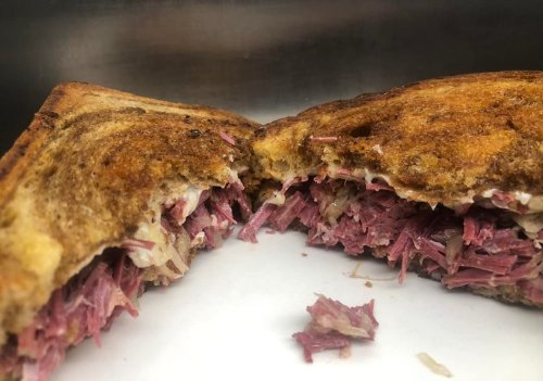 Close-up of a toasted sandwich filled with shredded meat and melted cheese, cut in half to reveal the filling.