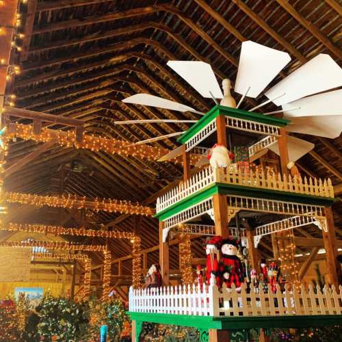 A festive barn interior decorated with lights, featuring a colorful carousel with holiday figures.