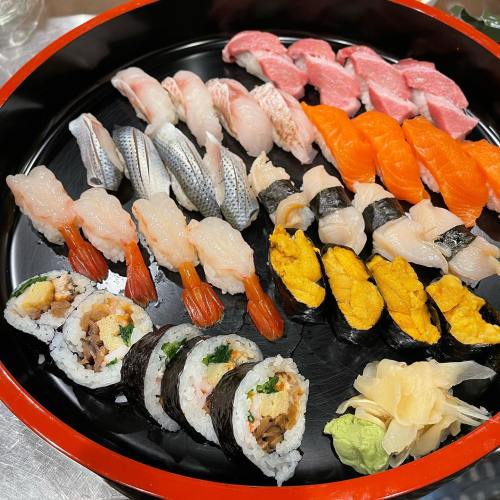 A colorful assortment of sushi and sashimi arranged on a black platter, featuring various fish and rolls.