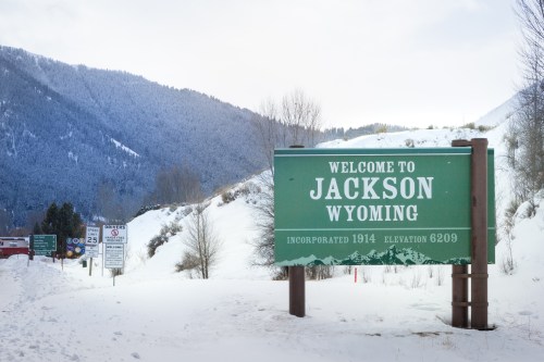 A welcome sign for Jackson, Wyoming, surrounded by snow-covered mountains and trees.