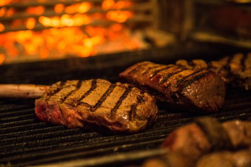 Grilled steaks with char marks cooking over an open flame, creating a warm, smoky atmosphere.