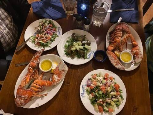 A table set with four plates of lobster, salads, and dipping sauce, surrounded by drinks and condiments.