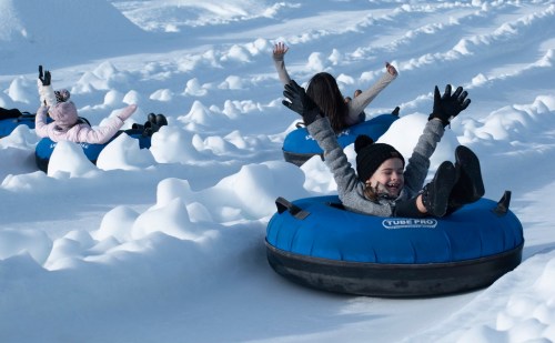 Children joyfully tubing down a snowy hill, with arms raised and smiles on their faces.