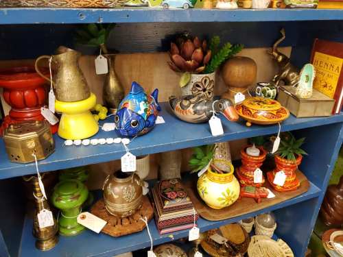 A colorful display of various decorative items and trinkets on a blue shelf, including pottery, figurines, and plants.