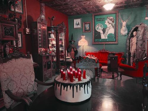 A vintage room with red walls, ornate furniture, a cake with candles, and eclectic decor, creating a spooky atmosphere.
