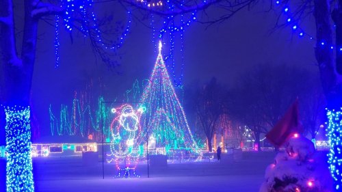 A snowy scene featuring colorful Christmas lights, including a large tree and festive decorations.