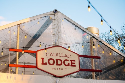 Sign for Cadillac Lodge in Detroit, with string lights illuminating a tent structure.