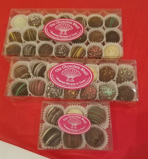 Three clear boxes filled with assorted chocolates, each with decorative toppings, on a red tablecloth.