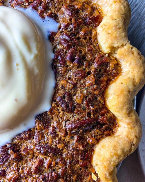 Close-up of a pecan pie topped with a scoop of vanilla ice cream, showcasing a golden crust and rich filling.