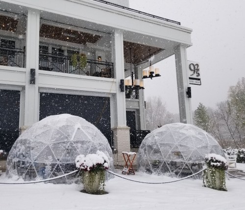 Two snow-covered igloos outside a restaurant, surrounded by snowflakes, with a sign reading "92°".