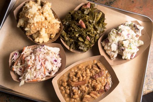 A tray with five servings of Southern-style sides: mashed potatoes, collard greens, potato salad, coleslaw, and baked beans.