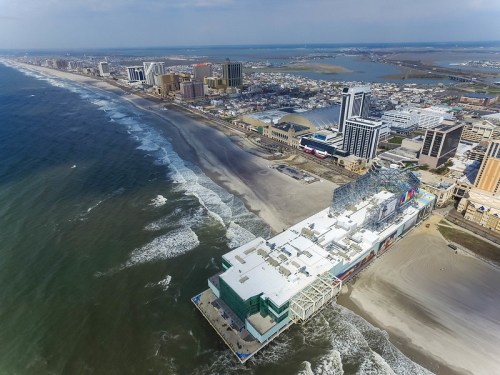 Aerial view of a coastal city with sandy beaches, waves, and modern buildings along the shoreline.