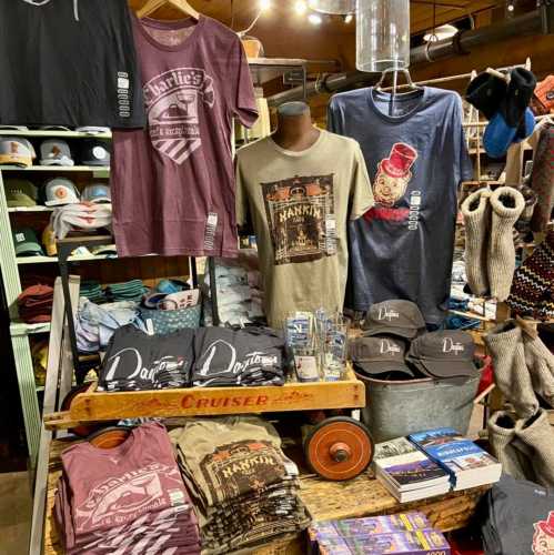 A display of various t-shirts and merchandise in a store, featuring colorful designs and a rustic setting.