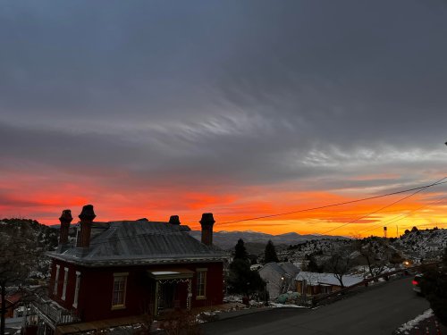 A vibrant sunset casts orange and pink hues over a snowy landscape, with a red house in the foreground.