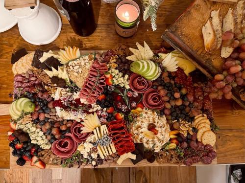 A beautifully arranged charcuterie board with meats, cheeses, fruits, nuts, and chocolates on a wooden table.