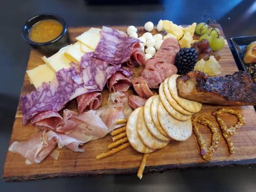 A wooden platter featuring assorted meats, cheeses, crackers, grapes, and a small bowl of mustard.