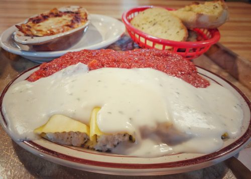 A plate of creamy chicken and dumplings topped with marinara sauce, served with garlic bread and a side of baked pasta.