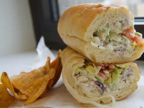 A sandwich filled with creamy chicken salad, lettuce, and tomatoes, served with a side of potato chips.