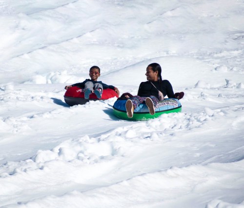 Two people sitting on snow tubes, enjoying a snowy slope on a bright day.