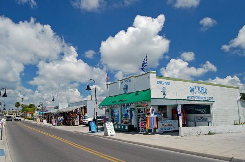 A vibrant street scene featuring shops with colorful awnings, under a bright blue sky with fluffy clouds.