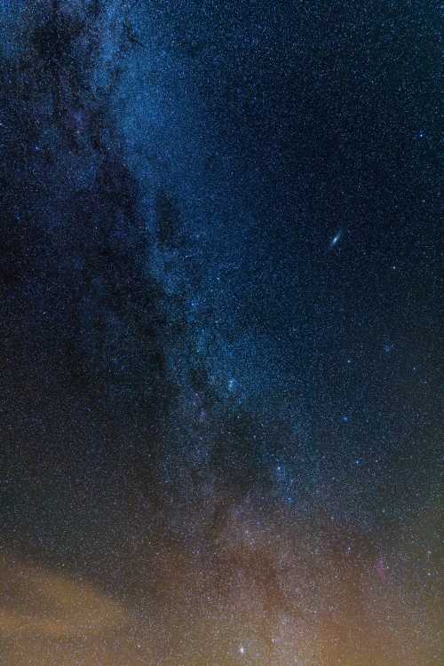 A stunning night sky filled with stars, showcasing the Milky Way and a distant galaxy against a dark backdrop.