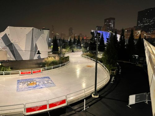A quiet outdoor ice skating rink at night, surrounded by city buildings and illuminated by soft lights.