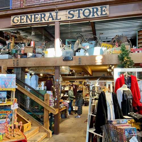 Interior of a rustic general store with wooden beams, shelves of goods, and shoppers browsing.