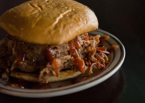 A close-up of a pulled pork sandwich topped with barbecue sauce on a plate.