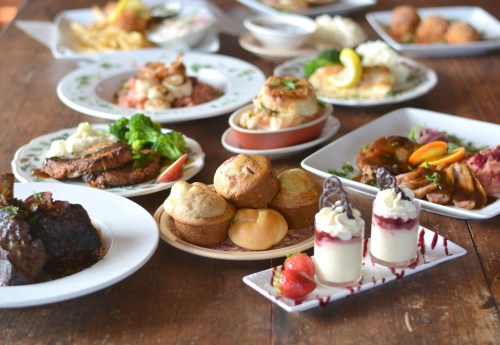 A table filled with various dishes, including meats, salads, muffins, and desserts, all beautifully presented.