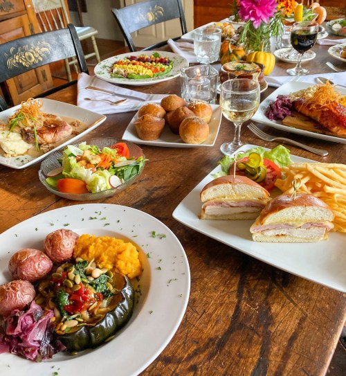 A festive table spread with various dishes, including salads, sandwiches, roasted meats, and colorful sides.