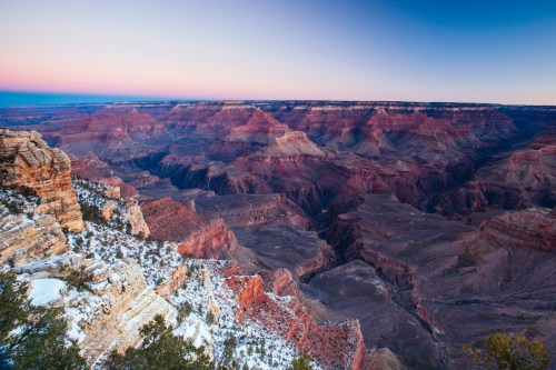 A panoramic view of the Grand Canyon at dawn, showcasing layered rock formations and a colorful sky.