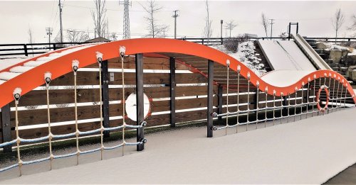 A colorful playground structure with a wavy design, surrounded by snow and featuring a slide in the background.