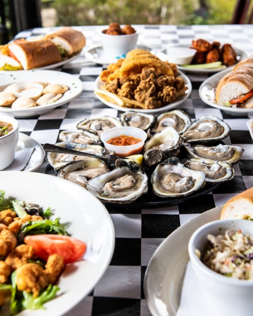 A table set with various dishes, including oysters, fried chicken, salads, and sandwiches on a checkered tablecloth.