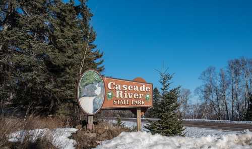 Sign for Cascade River State Park, surrounded by snow and trees, under a clear blue sky.