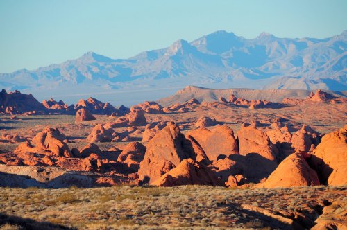 A vast desert landscape with red rock formations and distant mountains under a clear blue sky.
