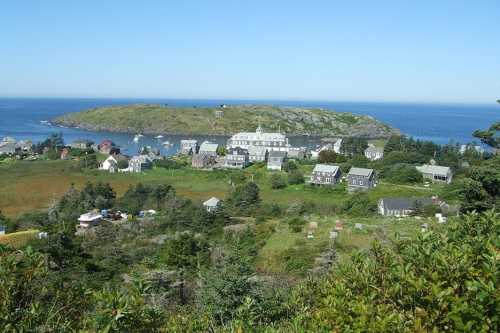 A scenic view of a coastal village with houses, greenery, and an island in the background under a clear blue sky.