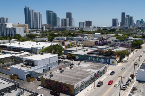 Aerial view of a vibrant urban area with murals, low-rise buildings, and tall skyscrapers in the background.