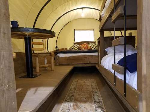 Cozy interior of a glamping tent featuring a bunk bed, a double bed, and a small dining table.