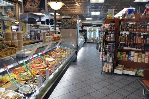 A vibrant deli interior showcasing a variety of prepared foods and shelves stocked with jars and canned goods.