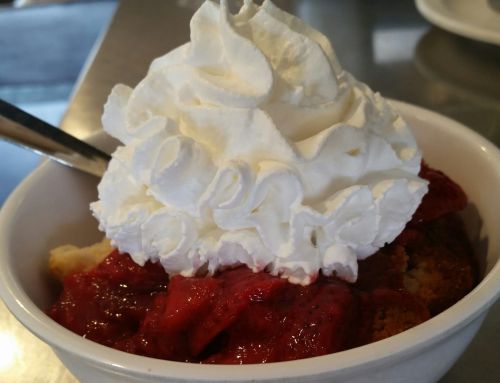A bowl of dessert topped with whipped cream and strawberry sauce over cake pieces.