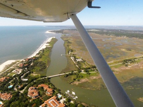 Aerial view of a coastal landscape with a river, marshes, and residential areas along the shore.