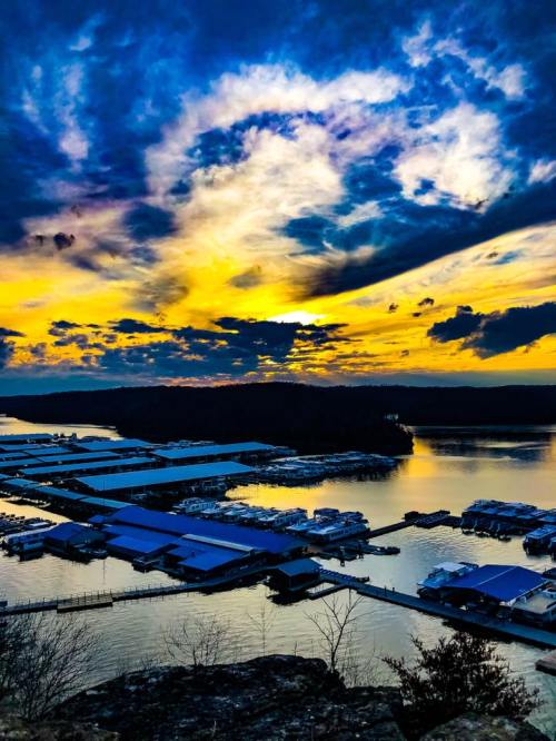 A vibrant sunset over a marina, with colorful clouds reflecting on the water and boats docked below.