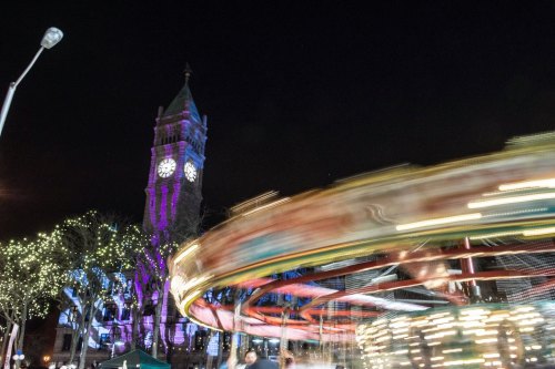 A brightly lit carousel spins at night, with a clock tower illuminated in the background.