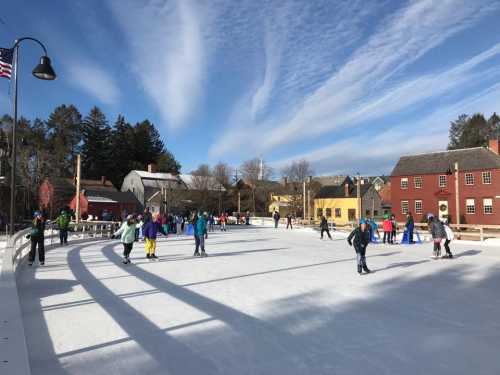 A bustling outdoor ice skating rink with people skating, surrounded by trees and colorful buildings under a blue sky.