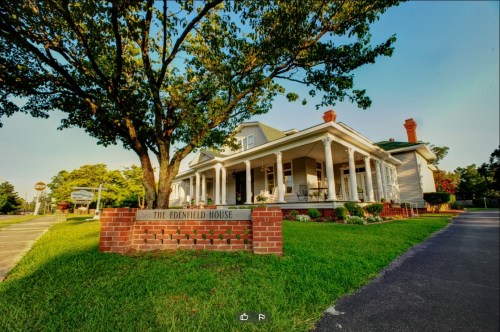 A charming white house with a porch, surrounded by greenery, featuring a sign that reads "The Edenfield House."
