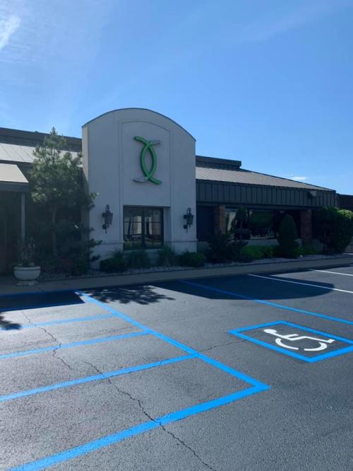 Exterior view of a building with a green logo, surrounded by landscaping and a blue sky. Parking lot visible in front.