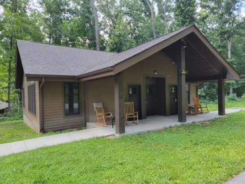 A cozy cabin with a porch, rocking chairs, and surrounded by lush greenery in a wooded area.