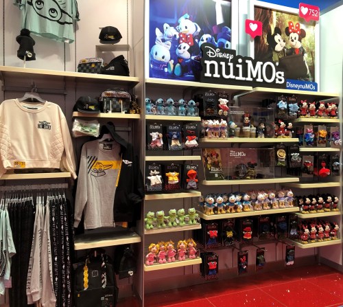 Display of Disney nuiMOs merchandise, including plush toys, clothing, and accessories on shelves.