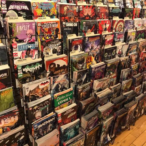 A display of various comic books organized on shelves, featuring titles from DC and Marvel, including Batman and Spider-Man.