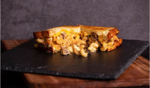 A grilled cheese sandwich filled with creamy macaroni and cheese, served on a slate plate.